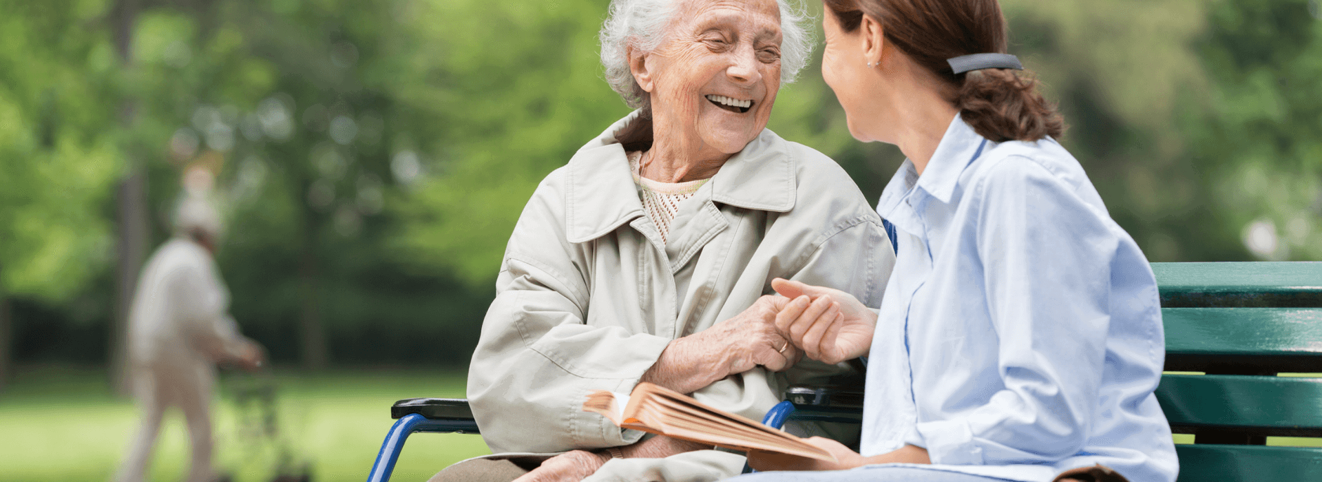 An elderly woman and her carer sat on a bench