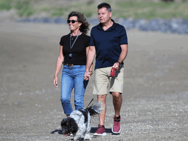 Man and woman walking along beach with dog
