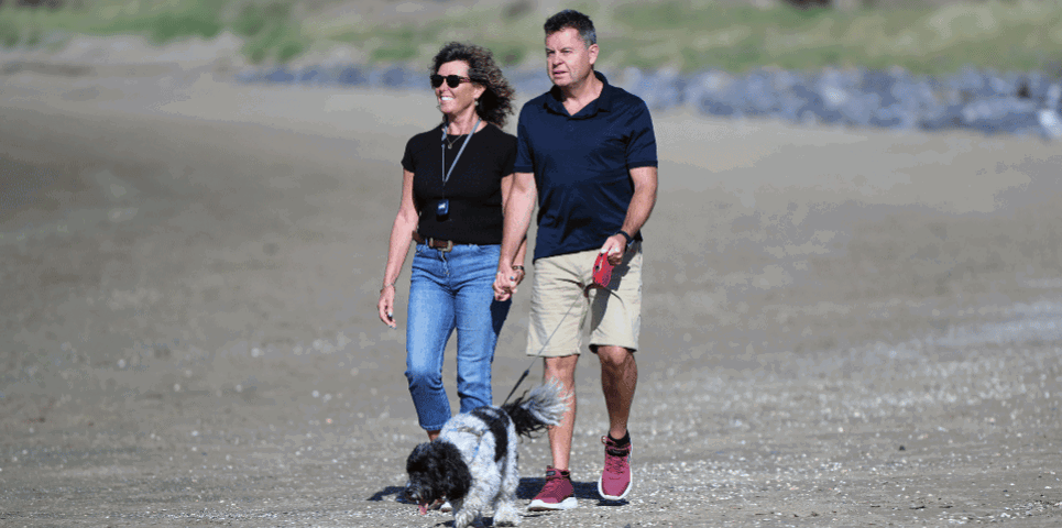 Man and woman walking along beach with dog