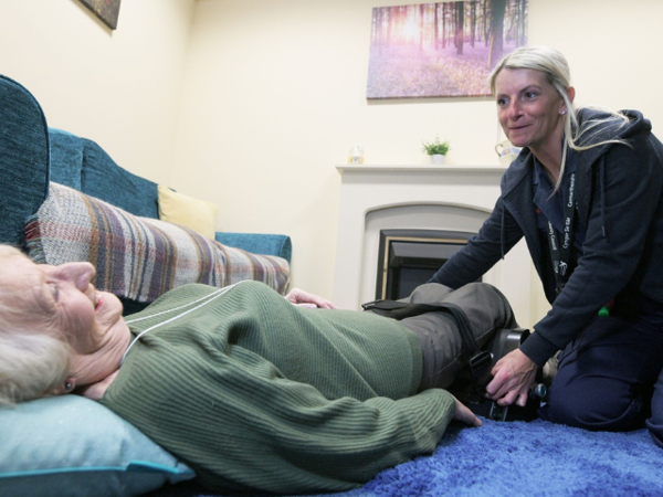 A Delta carer helping an older woman get up safely from the floor using a lifting device