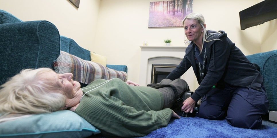 A Delta carer helping an older woman get up safely from the floor using a lifting device