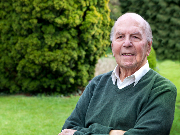 Person sitting in a garden with green lawns and hedges in the background.