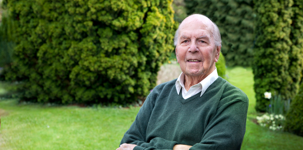 Person sitting in a garden with green lawns and hedges in the background.